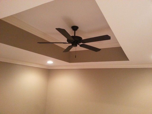 A dark brown five-blade ceiling fan installed in a tray ceiling with beige-colored walls and white trim.