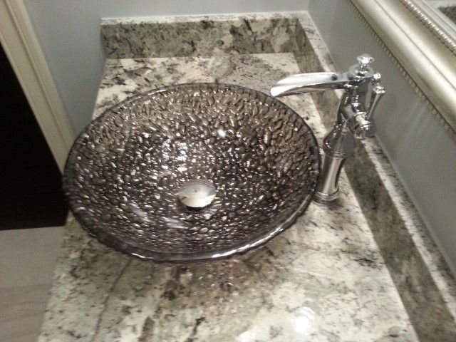 A circular, textured bronze glass vessel sink sits on a speckled granite countertop next to a chrome faucet.