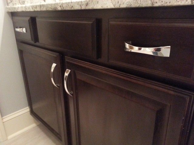 Dark wood bathroom vanity cabinets with silver handles and a granite countertop.
