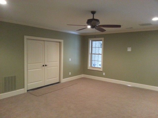 An empty room with sage green walls, white trim, beige carpet, double white doors, and a ceiling fan.