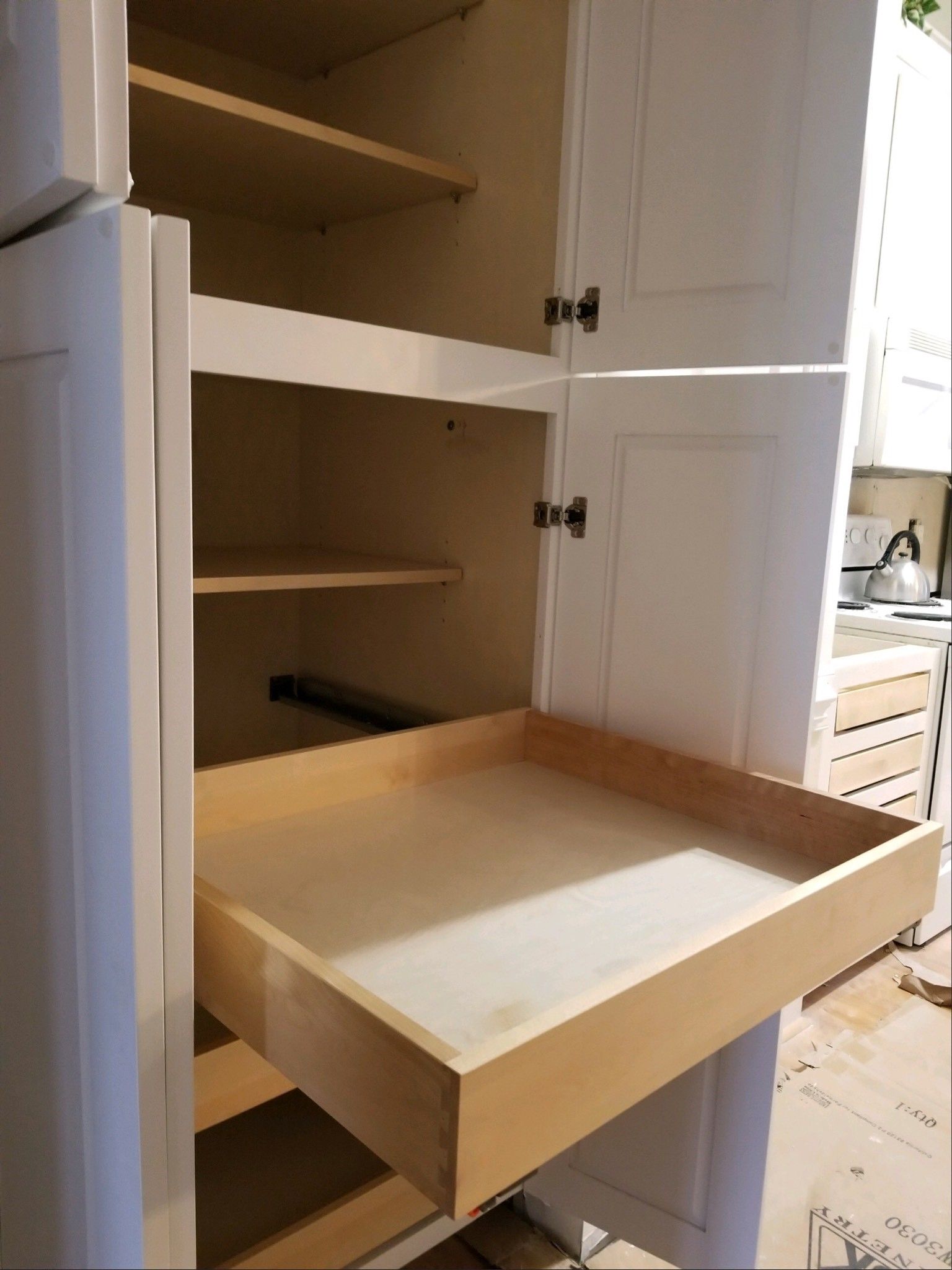 Open white pantry cabinet with a wooden pull-out drawer extended in a kitchen setting.