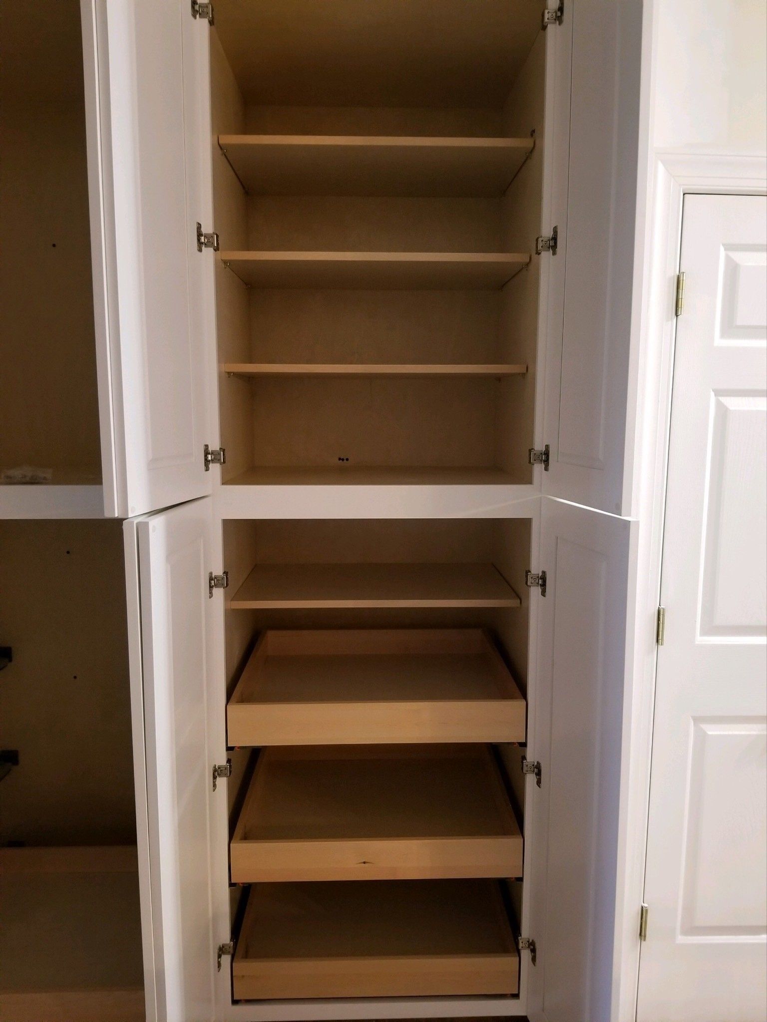 A tall, white kitchen pantry cabinet with open doors, featuring three fixed upper shelves and three sliding lower drawers.
