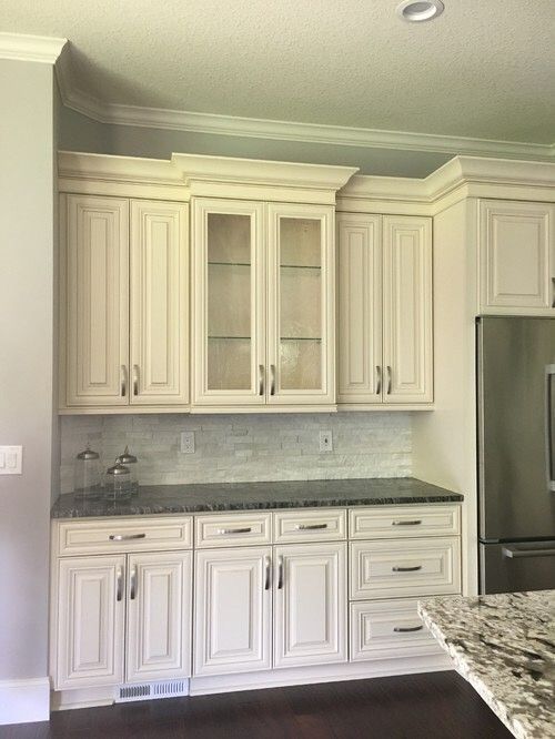 Off-white kitchen cabinets with glass-front center doors, a dark granite countertop, and light tile backsplash.