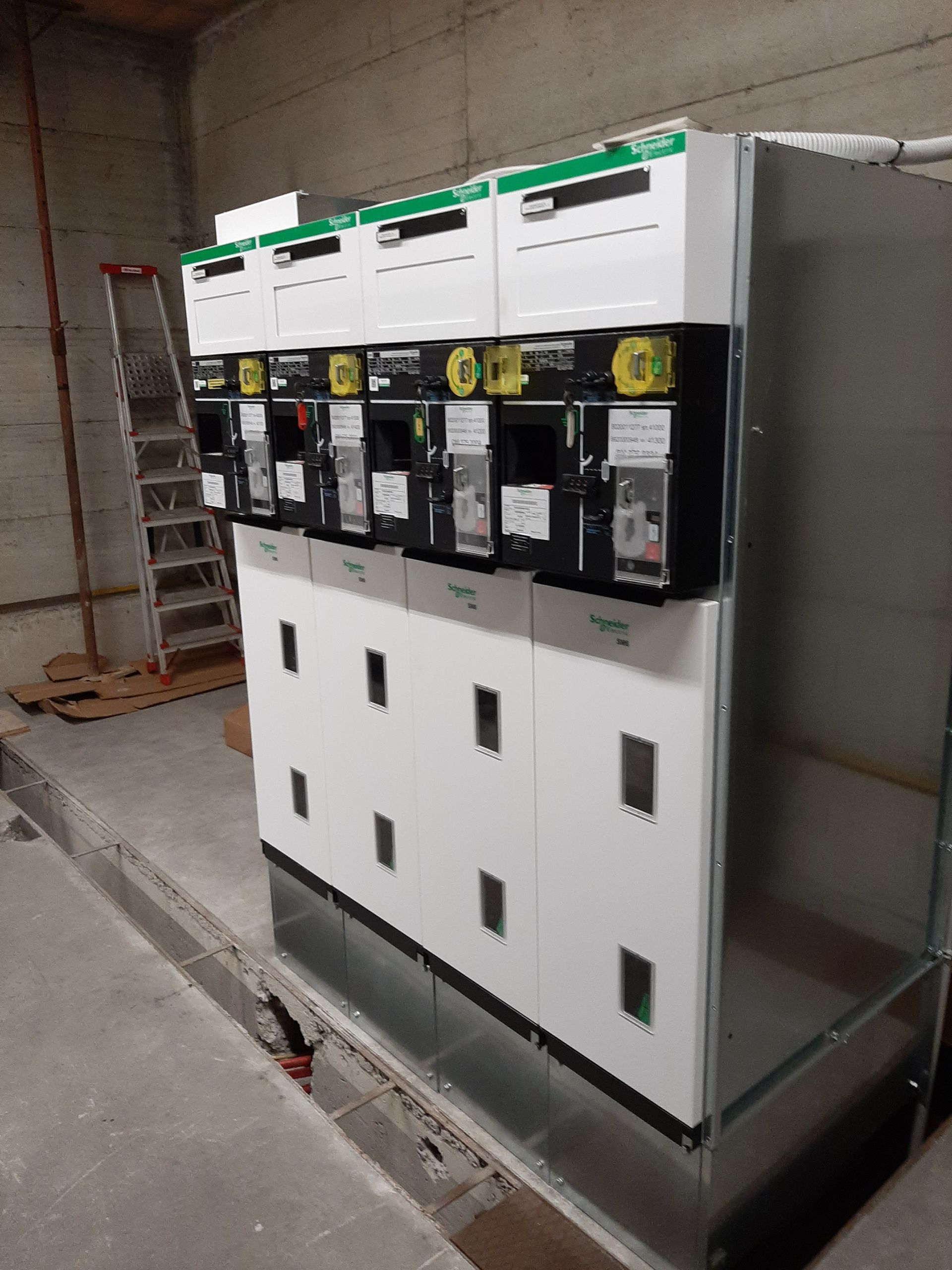 Armadi per quadri elettrici in un locale tecnico in cemento, con pannelli ed etichette in bianco e nero sulla parte superiore.