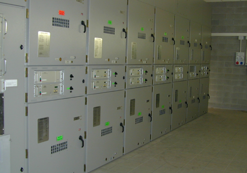 Una fila di armadi elettrici grigi per il controllo in un locale industriale con pavimento piastrellato.