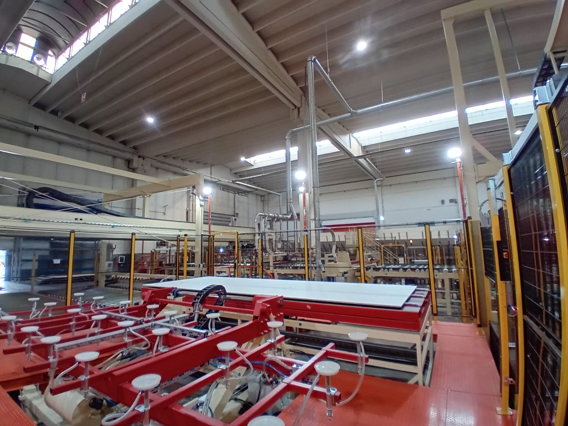 All'interno di un grande magazzino, in un ambiente industriale caratterizzato da macchinari rossi, strutture metalliche e luci a soffitto.