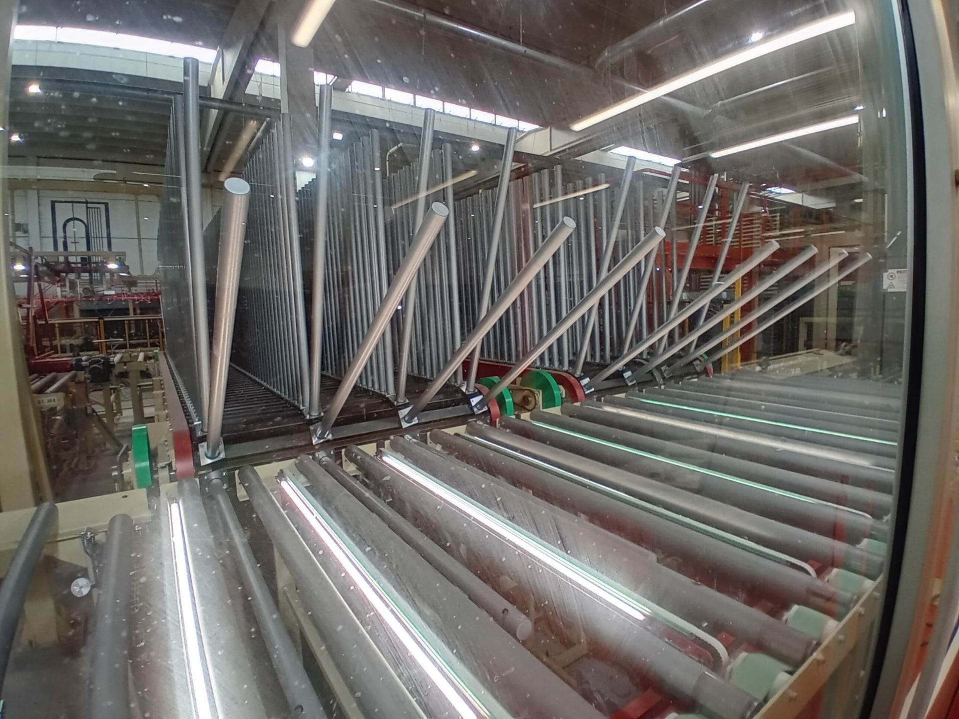 Sistema di trasporto industriale con rulli argentati e telai metallici all'interno di un'area di assemblaggio in fabbrica.