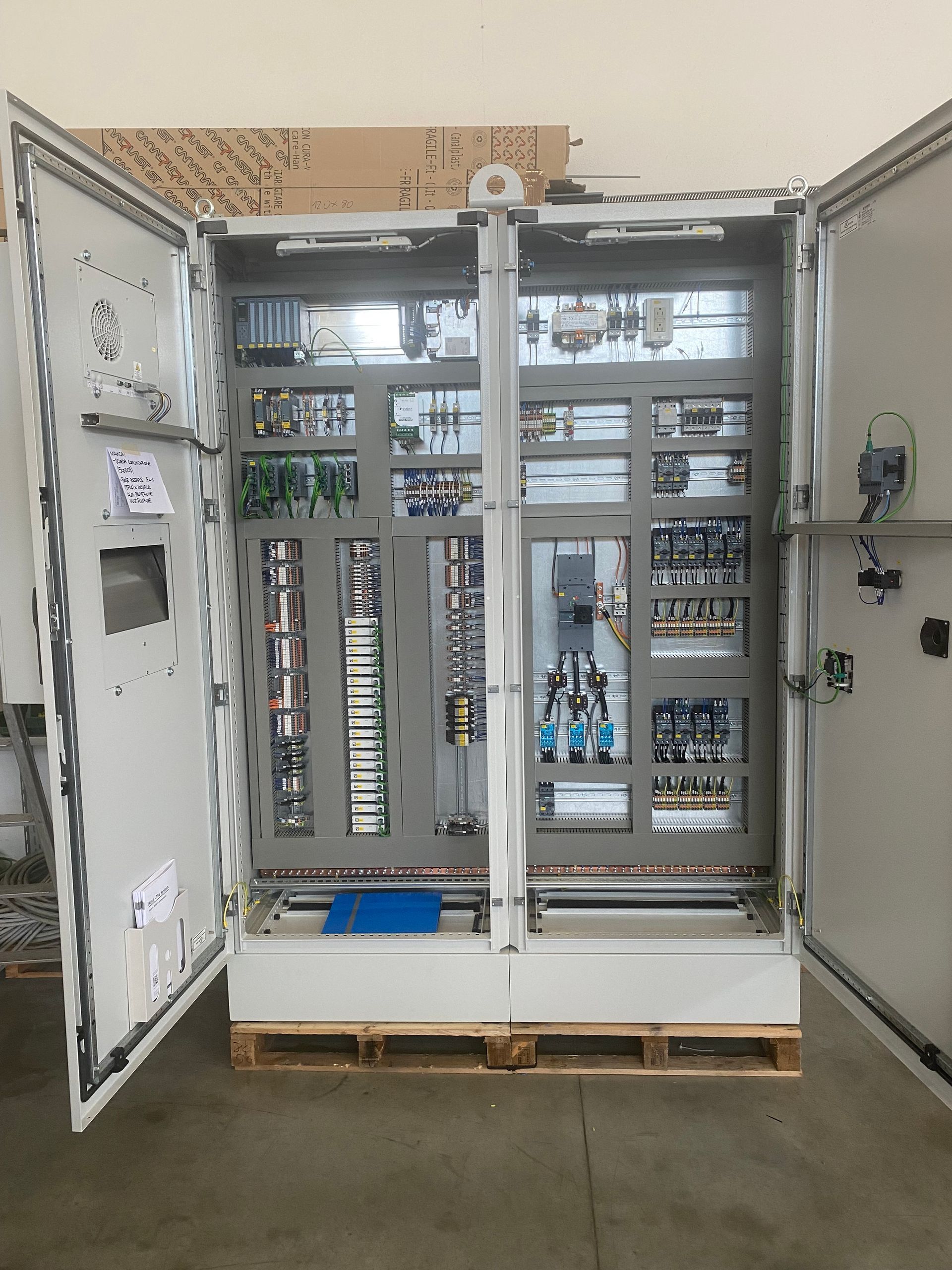 Quadro elettrico aperto con cablaggi e interruttori automatici in un'officina.