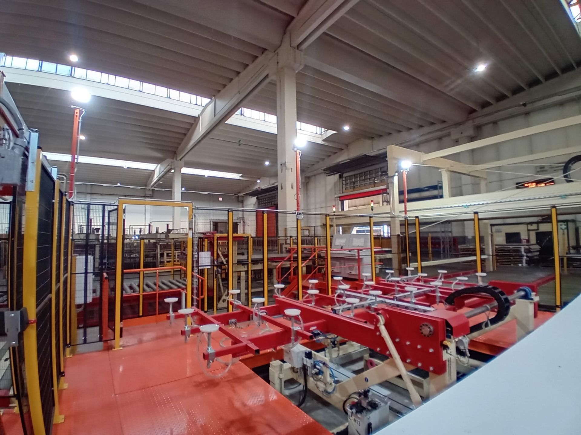 Interno di uno stabilimento industriale con macchinari rossi e ringhiere di sicurezza gialle sotto luci intense.