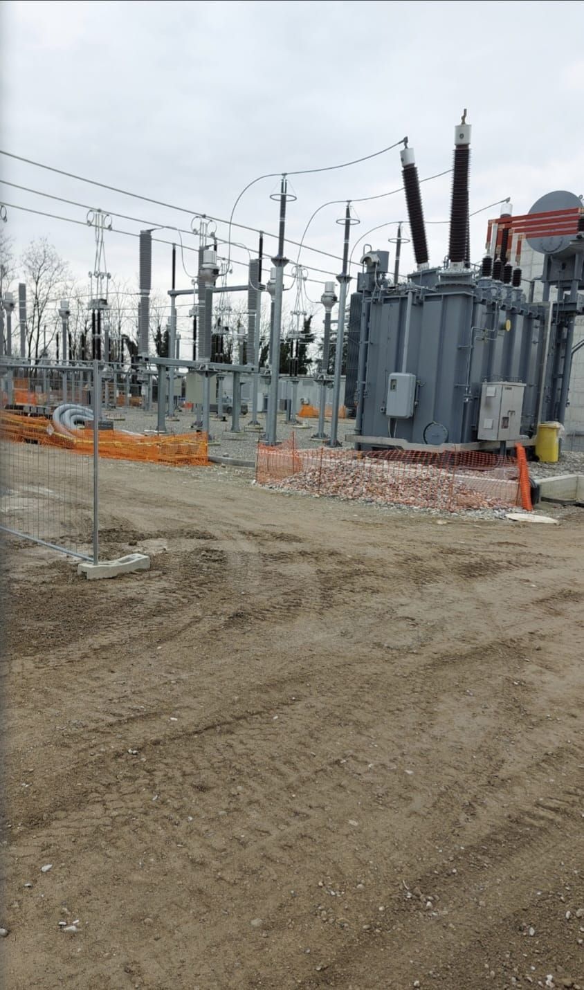 Sottostazione elettrica con trasformatori e linee elettriche grigie sullo sfondo di un terreno sterrato.