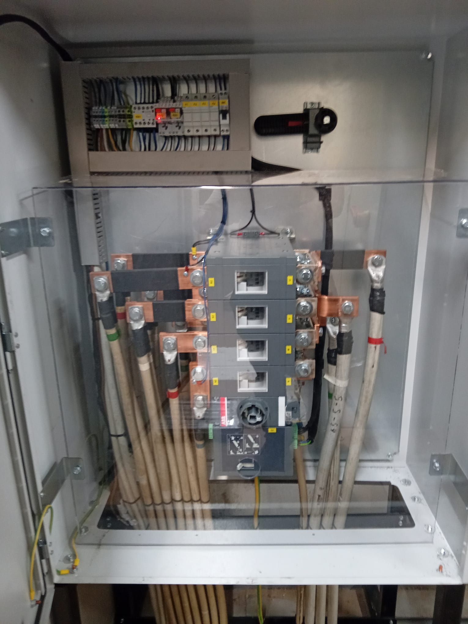 Quadro elettrico aperto con scatole dei fusibili, cavi e canaline all'interno di un armadio metallico.