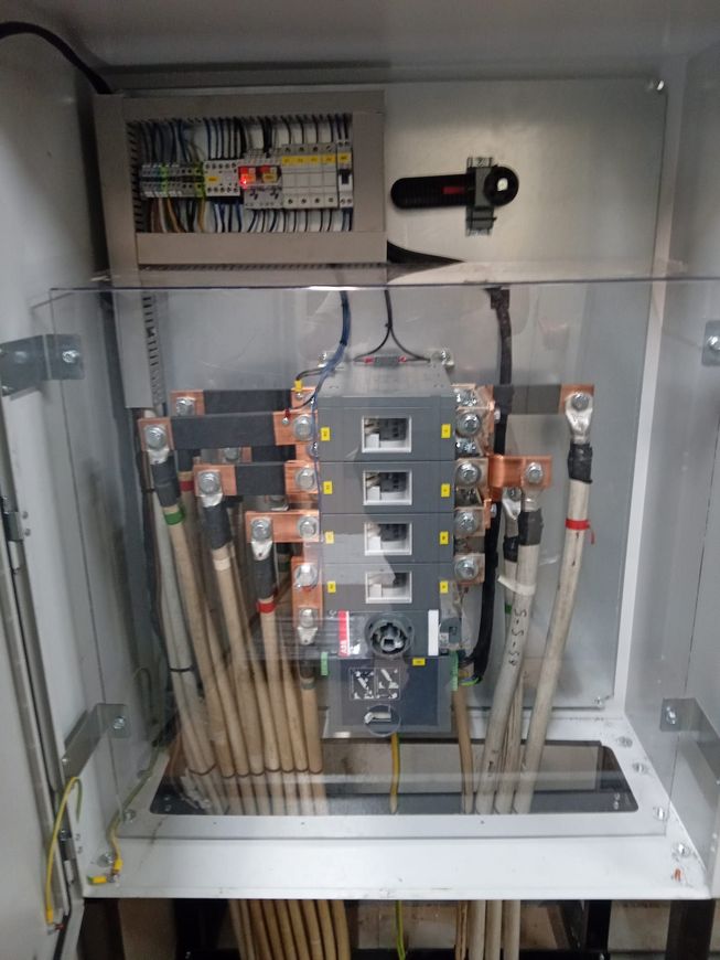 Quadro elettrico aperto con scatole dei fusibili, cavi e canaline all'interno di un armadio metallico.