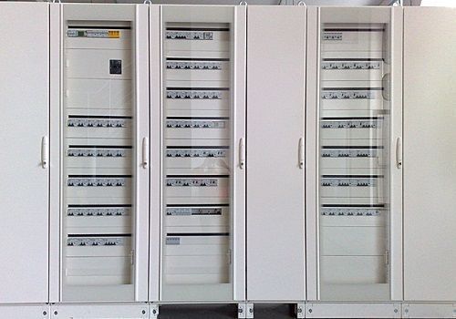 Armadi di controllo elettrico bianchi con ante in vetro e file di interruttori in un locale tecnico.