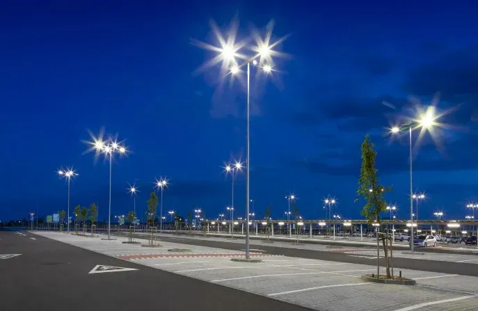 Parcheggio vuoto al crepuscolo, illuminato dai lampioni e con un cielo azzurro.