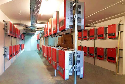 File di pannelli di controllo elettrici rossi in un lungo corridoio industriale, con una struttura metallica centrale.