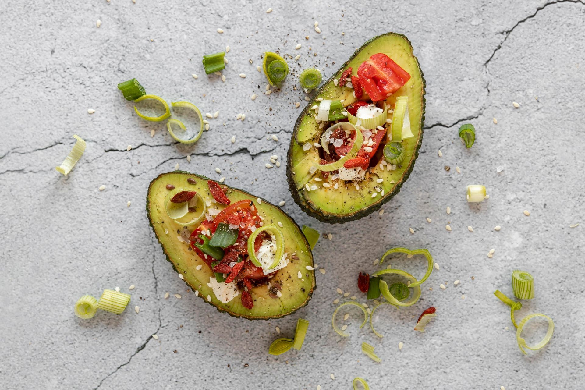 Dos mitades de aguacate rellenas de verduras sobre una mesa.