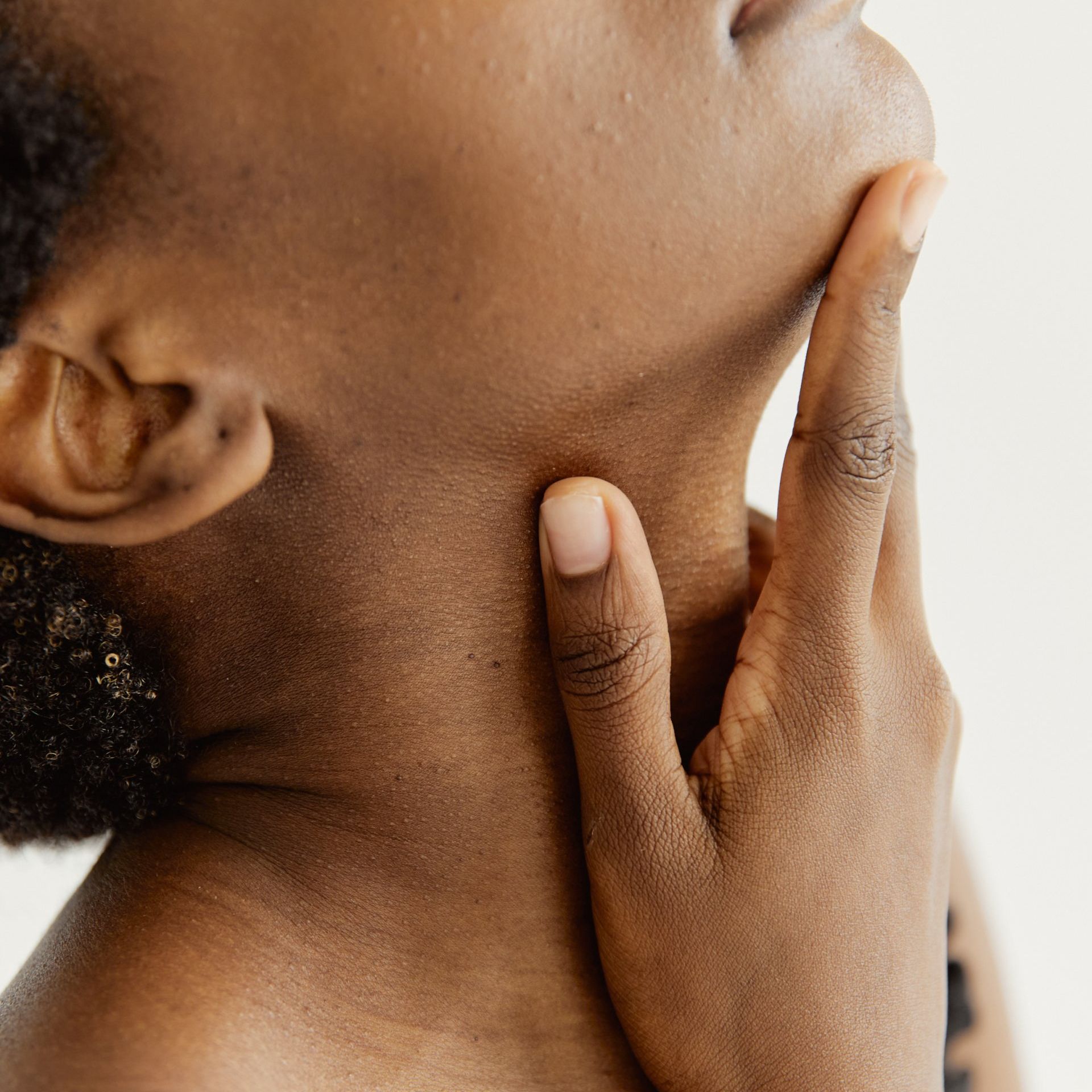 Un primer plano del cuello de una persona con su mano sobre él.