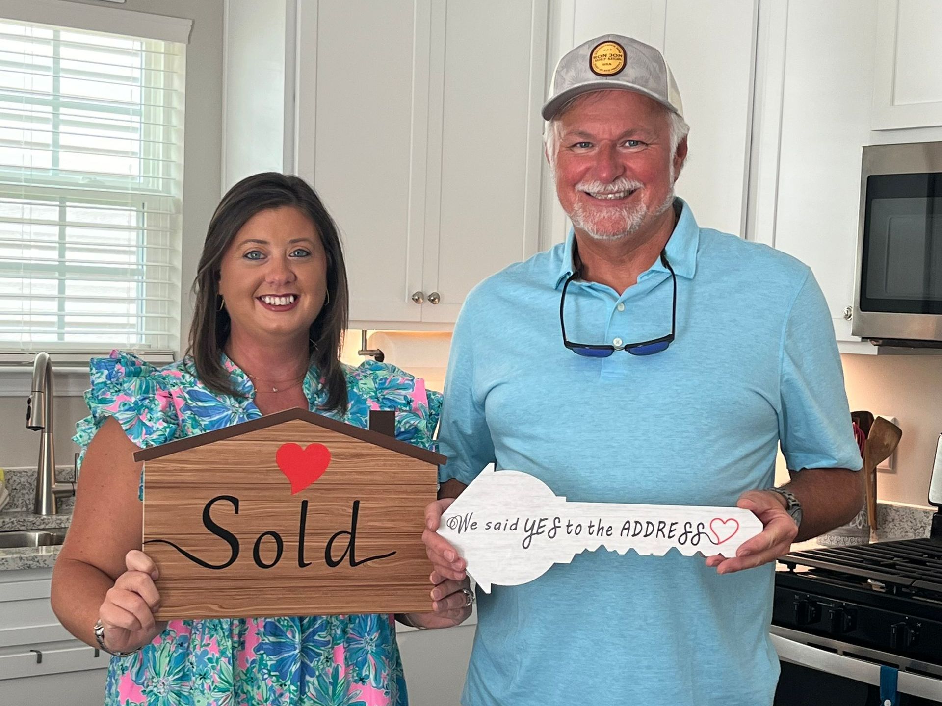 A man and a woman are holding a sold sign and a key in a kitchen.
