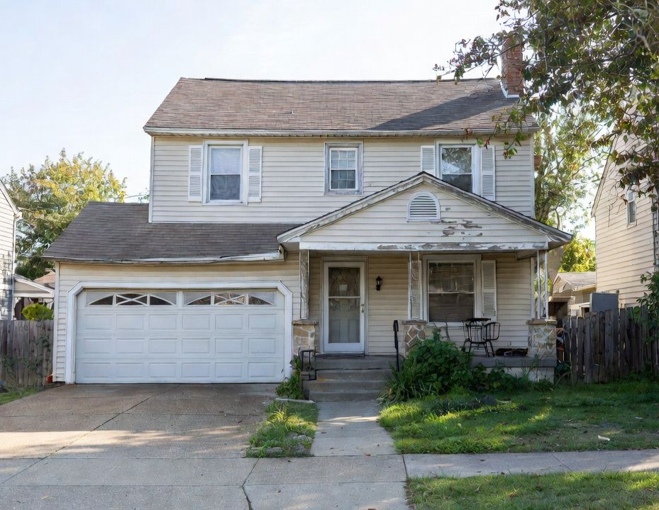Suburban two-story beige house with attached garage, driveway, porch, and front lawn