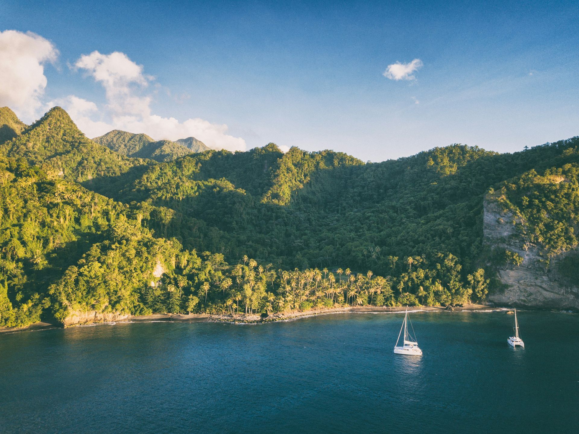 A couple of sailboats are floating on top of a body of water surrounded by mountains.