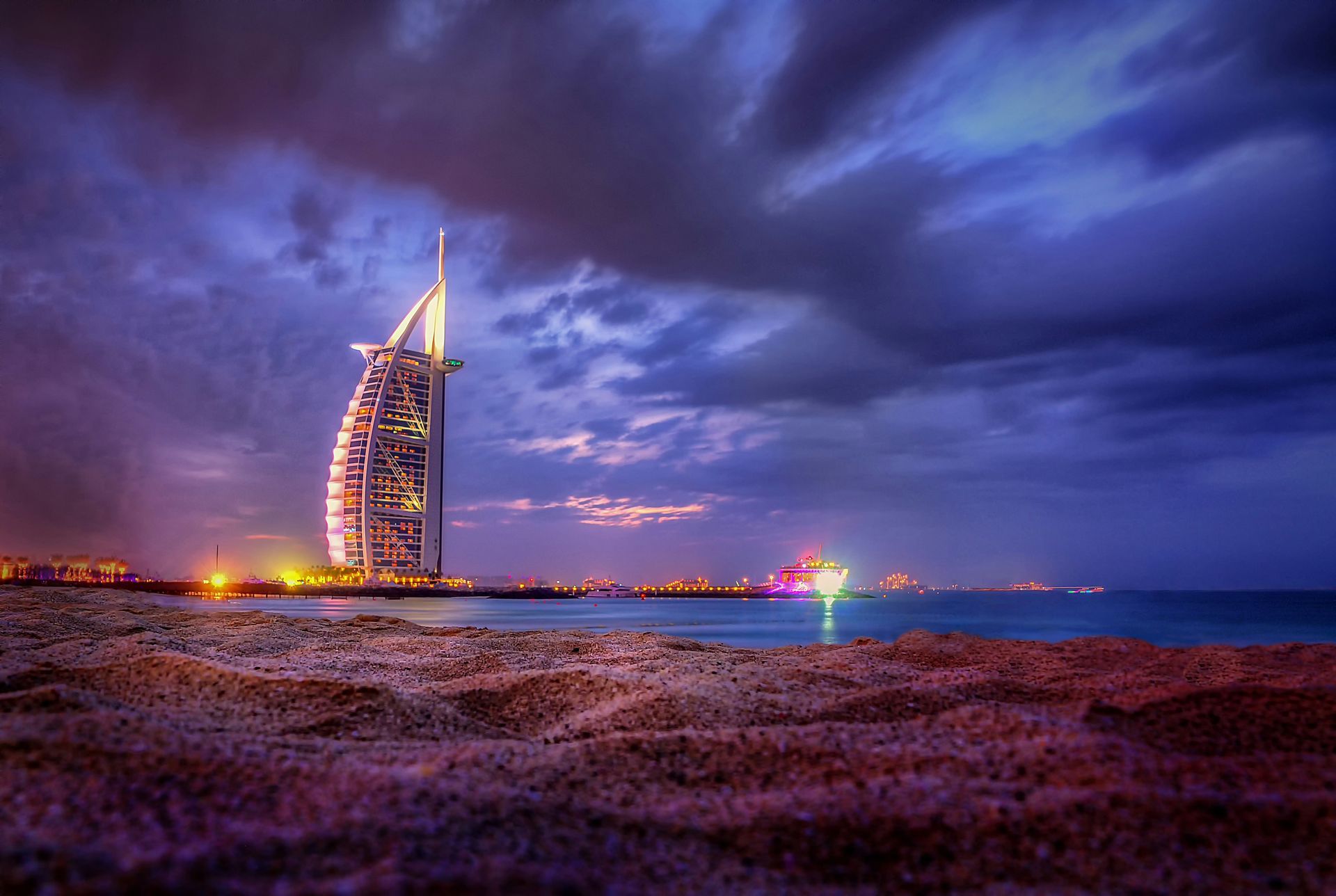 A large building is sitting on top of a sandy beach next to the ocean at night.