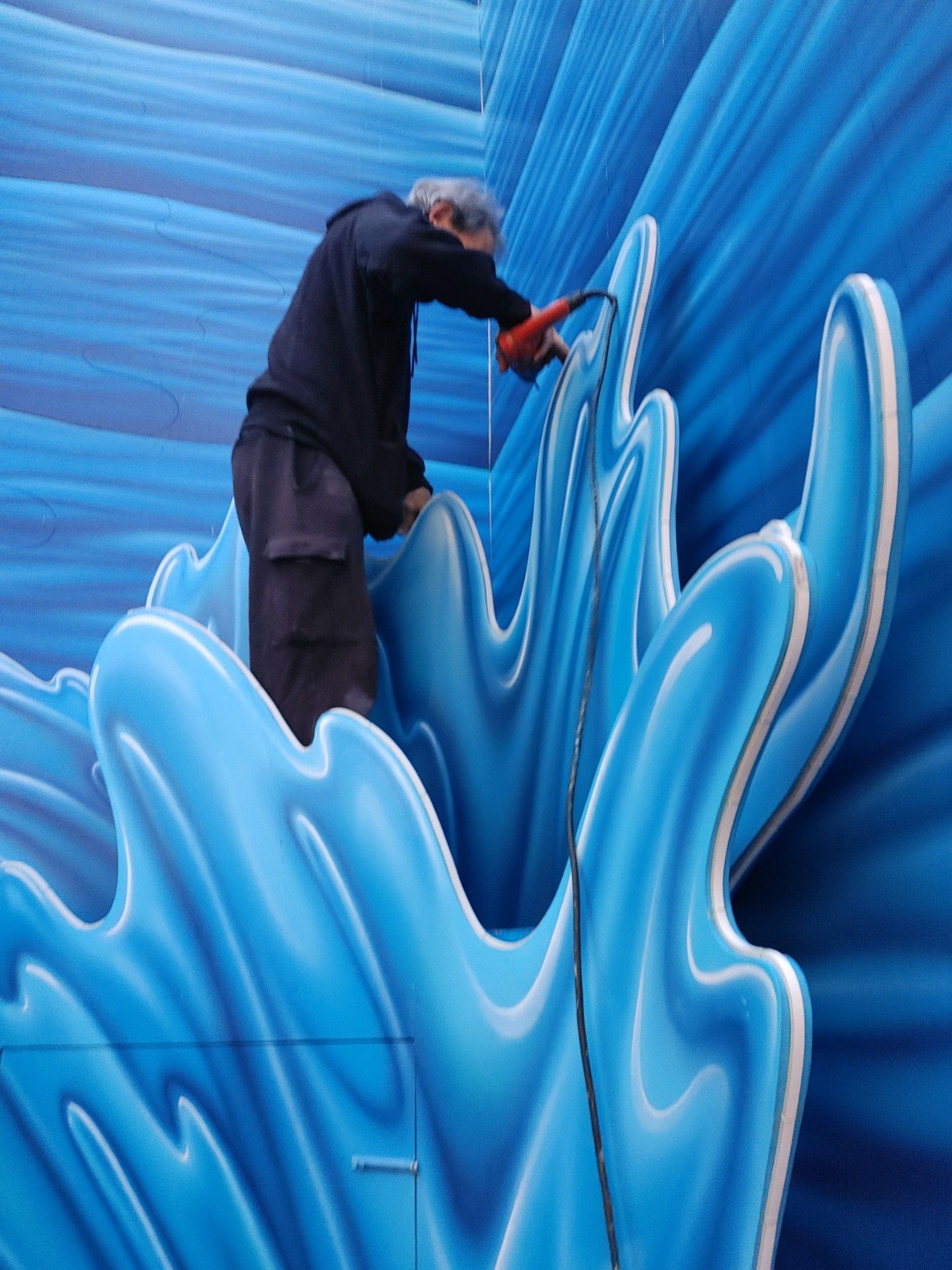 A person painting a bright blue mural with flowing abstract shapes on a wall