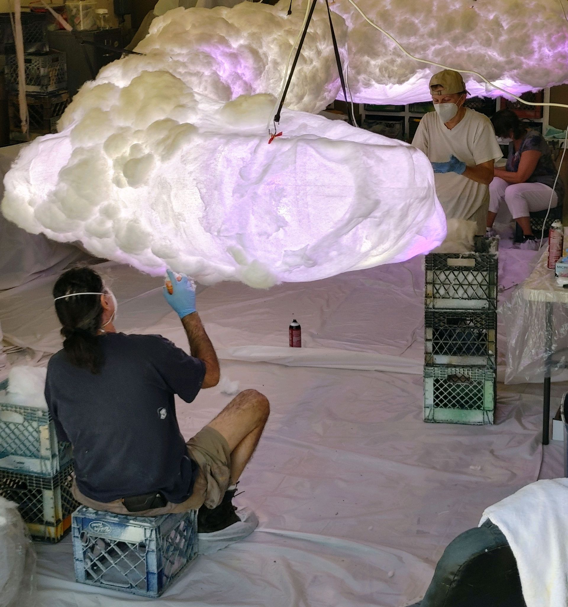 People seated under large glowing cloud sculptures in a pink-lit art installation