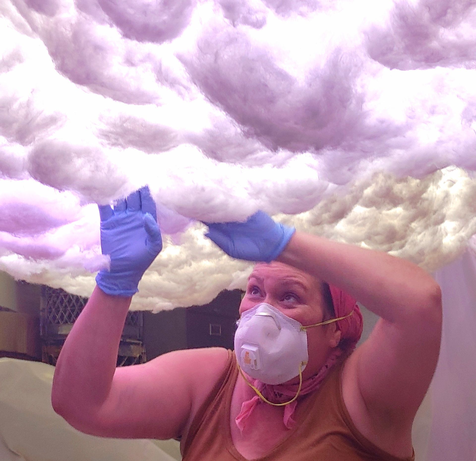 Person in gloves and mask adjusting fluffy white and lavender cloud-like material overhead.