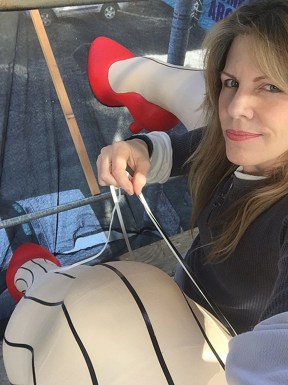 Woman in black tights and red heels sitting on a swing, holding the chains and looking at the camera.