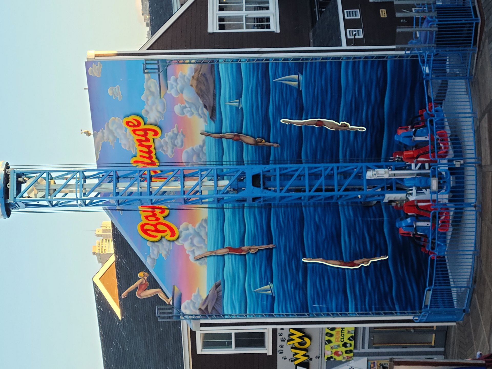 Blue water ride at an amusement park with a tall tower, suspended boats, and colorful signage