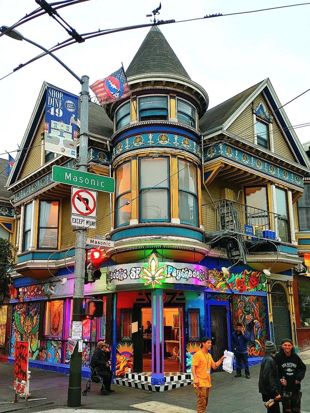 Colorful corner building with a turret, neon signs, and pedestrians on a city street.