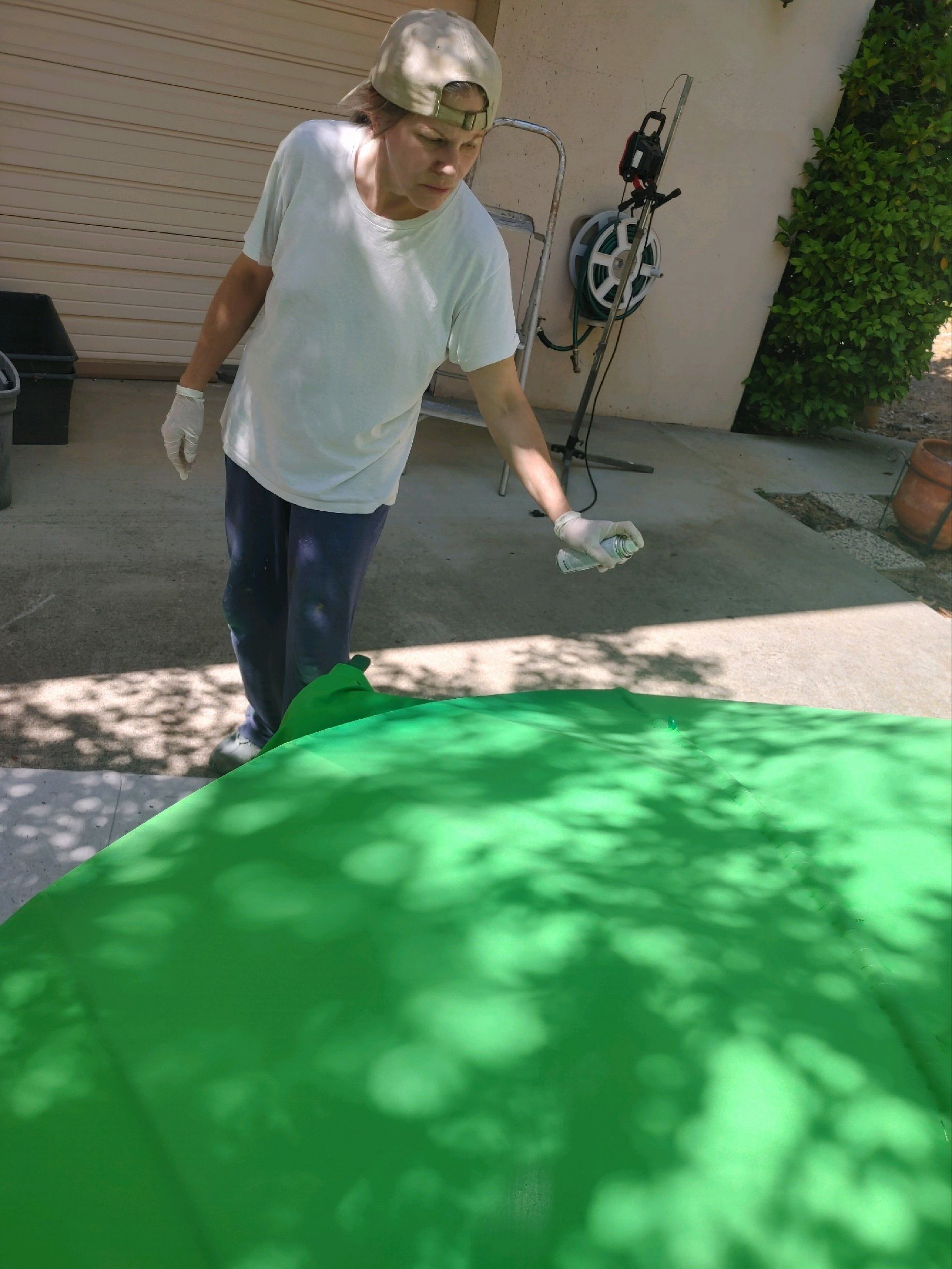 Person spray-painting a bright green round surface outdoors in a sunny driveway