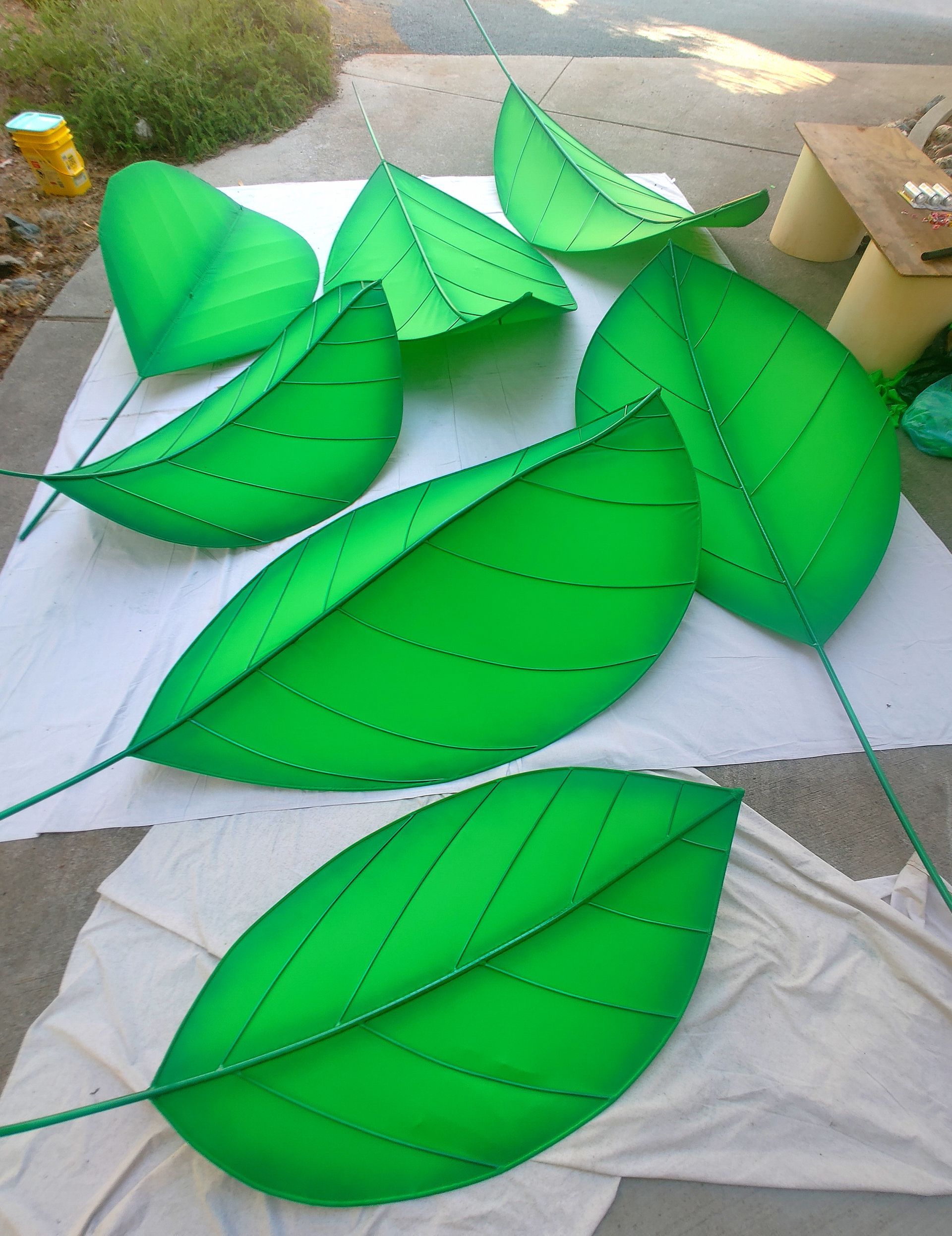 Green leaf-shaped craft pieces arranged on a table outdoors, with one large leaf in the foreground.