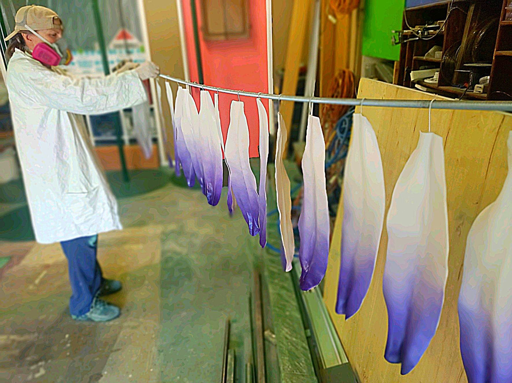 Person in a workshop hanging purple-and-white fabric pieces on a drying line