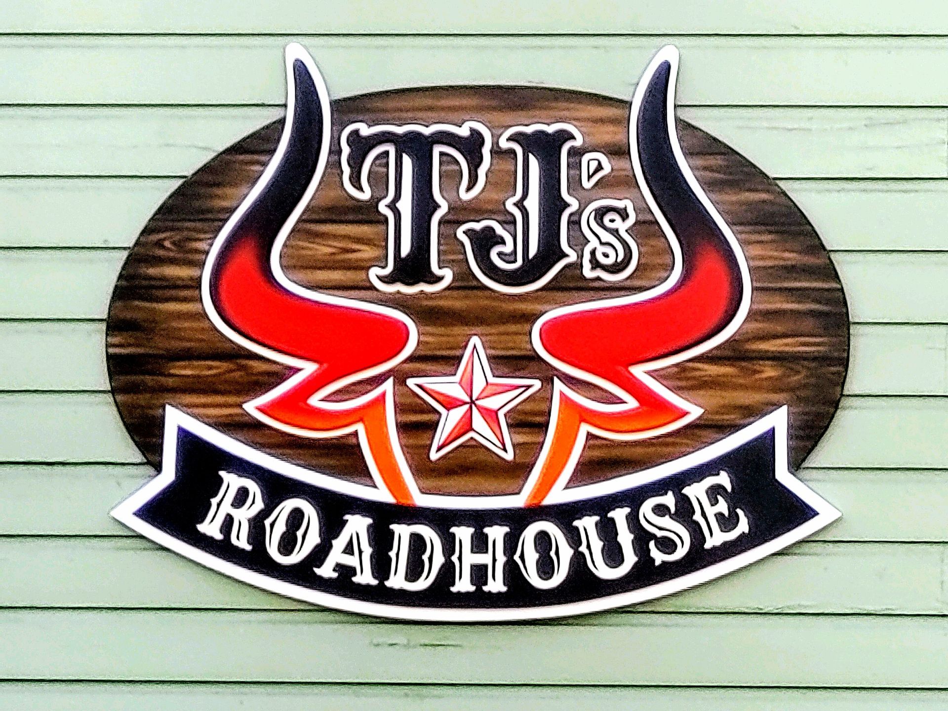 TJ’s Roadhouse logo with red bull horns and star on a wooden oval sign