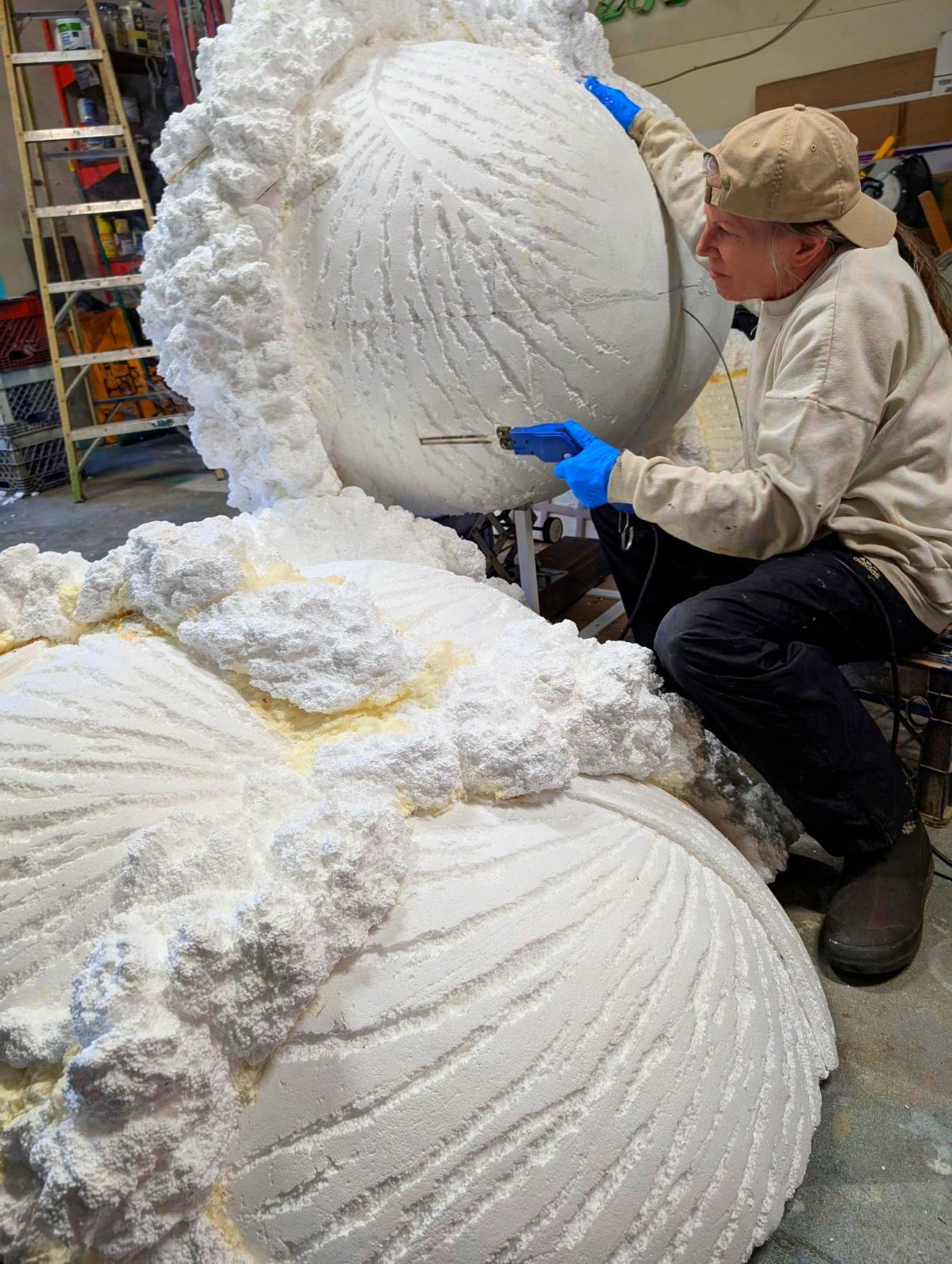 Worker carving large white foam sculpture in a workshop