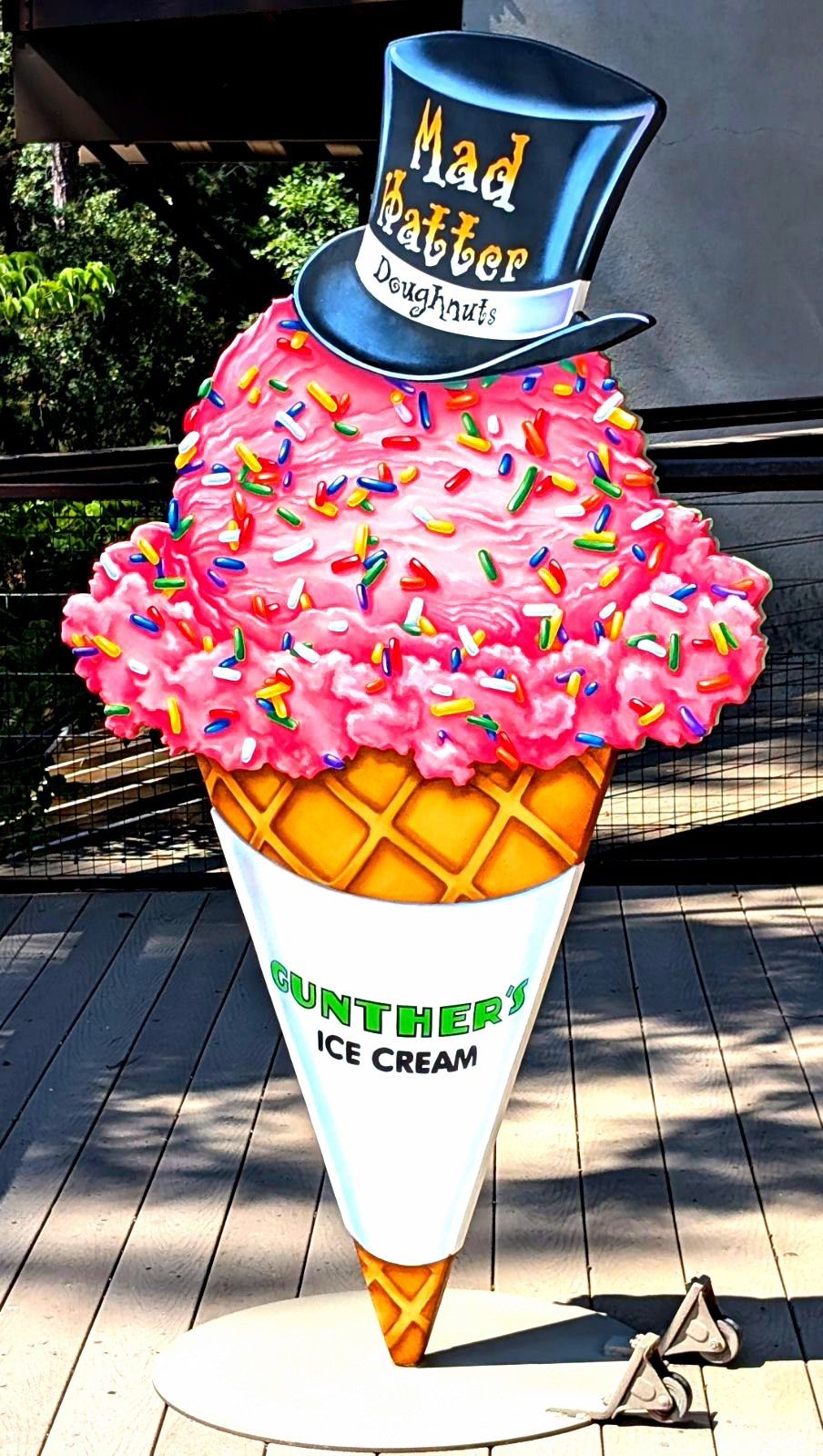 Giant pink-sprinkled ice cream cone statue with a blue hat, displayed outdoors on a sidewalk