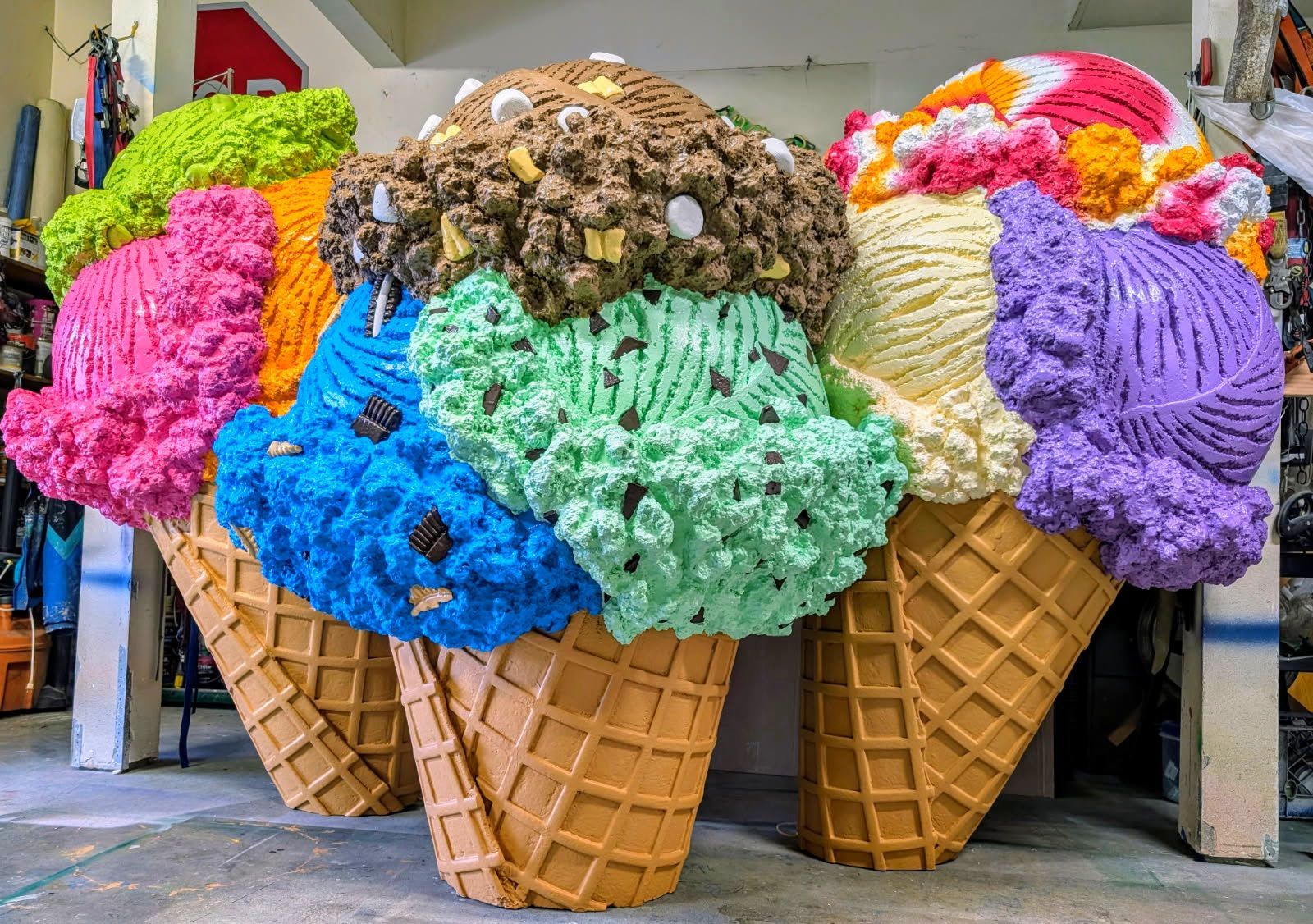 Oversized colorful ice cream cone sculptures outside a shop, with pink, blue, green, brown, purple, and orange scoops