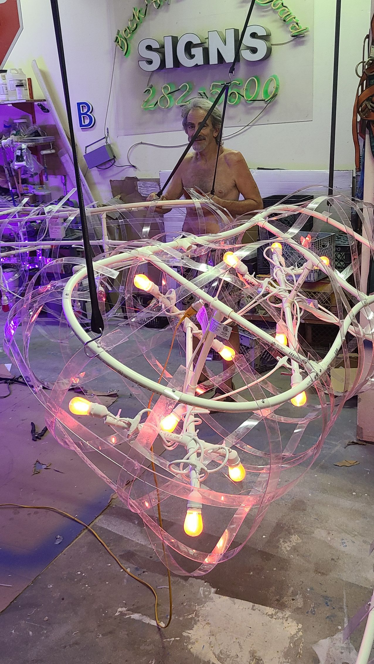 Person behind a glowing geometric light sculpture in a sign shop with purple lighting.