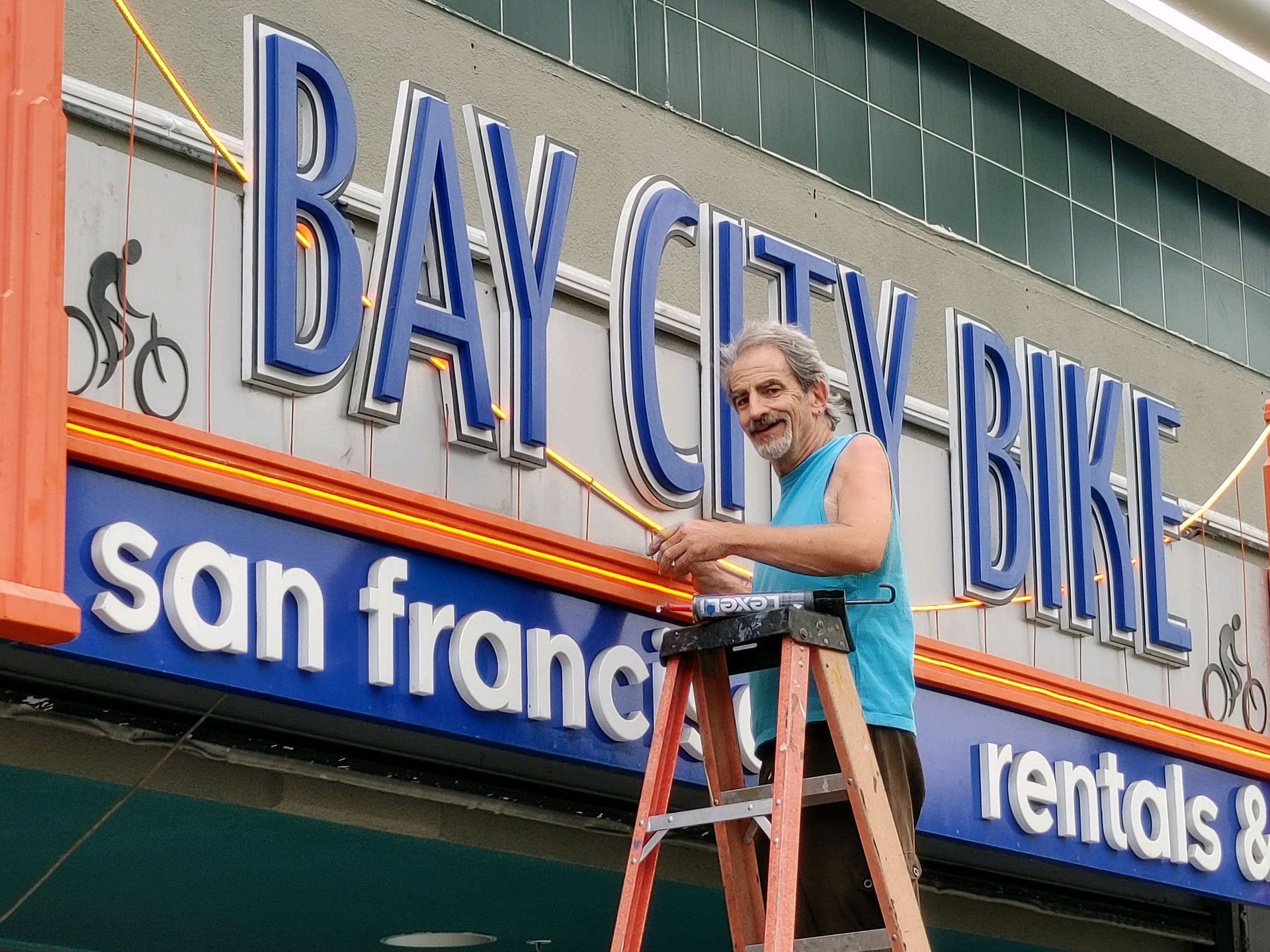 Person on a ladder painting the Bay City Bike San Francisco rentals sign