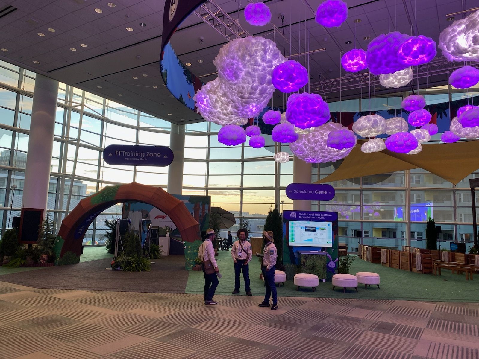 Purple hanging lights in a modern lobby, with a few people standing near a display and seating area.