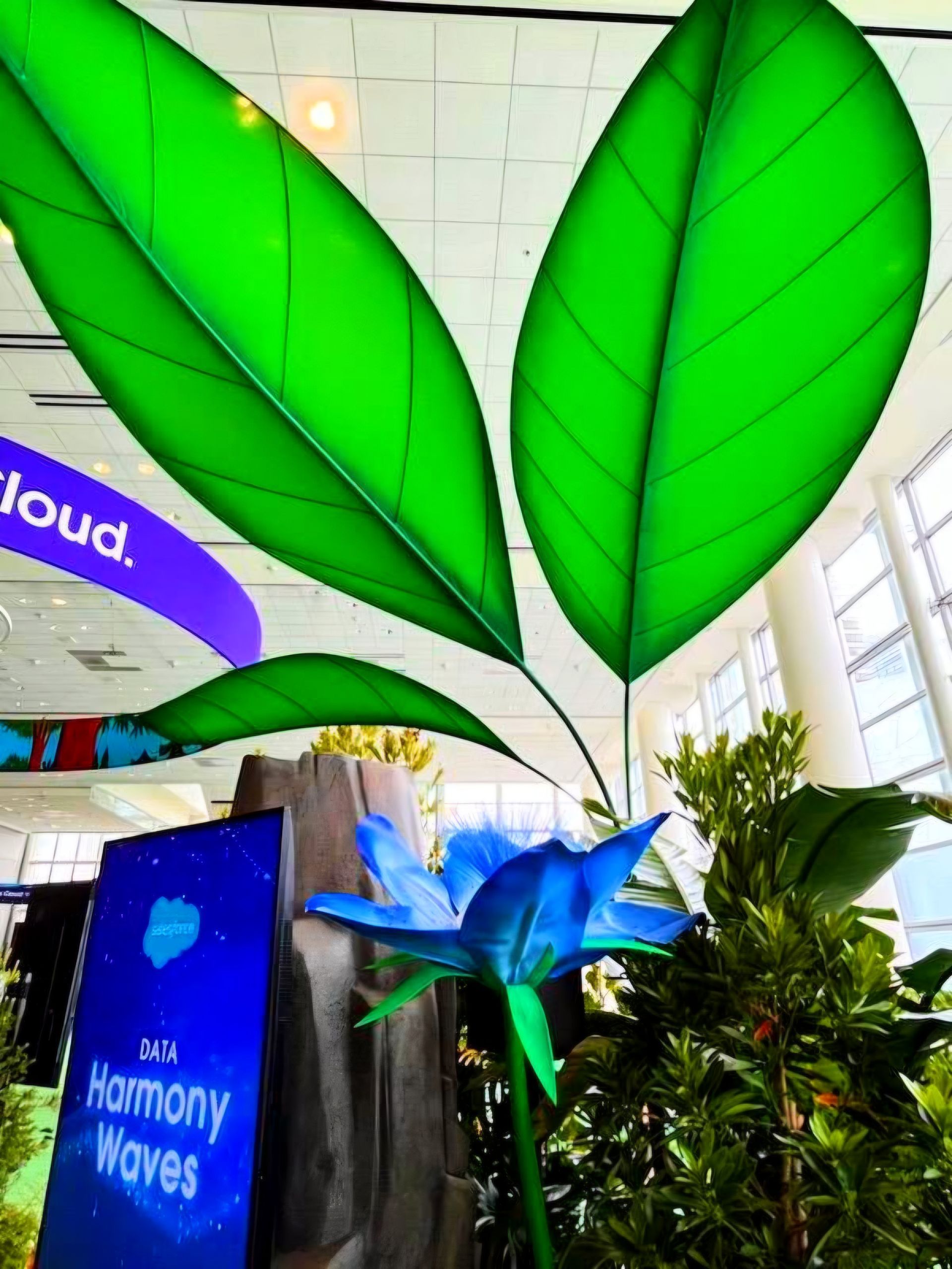 Large green leaf decorations in an indoor exhibition with a blue flower display and signage.