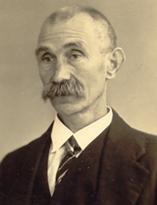 Sepia-getint portret van een man met snor in pak en stropdas, die iets naar links kijkt.