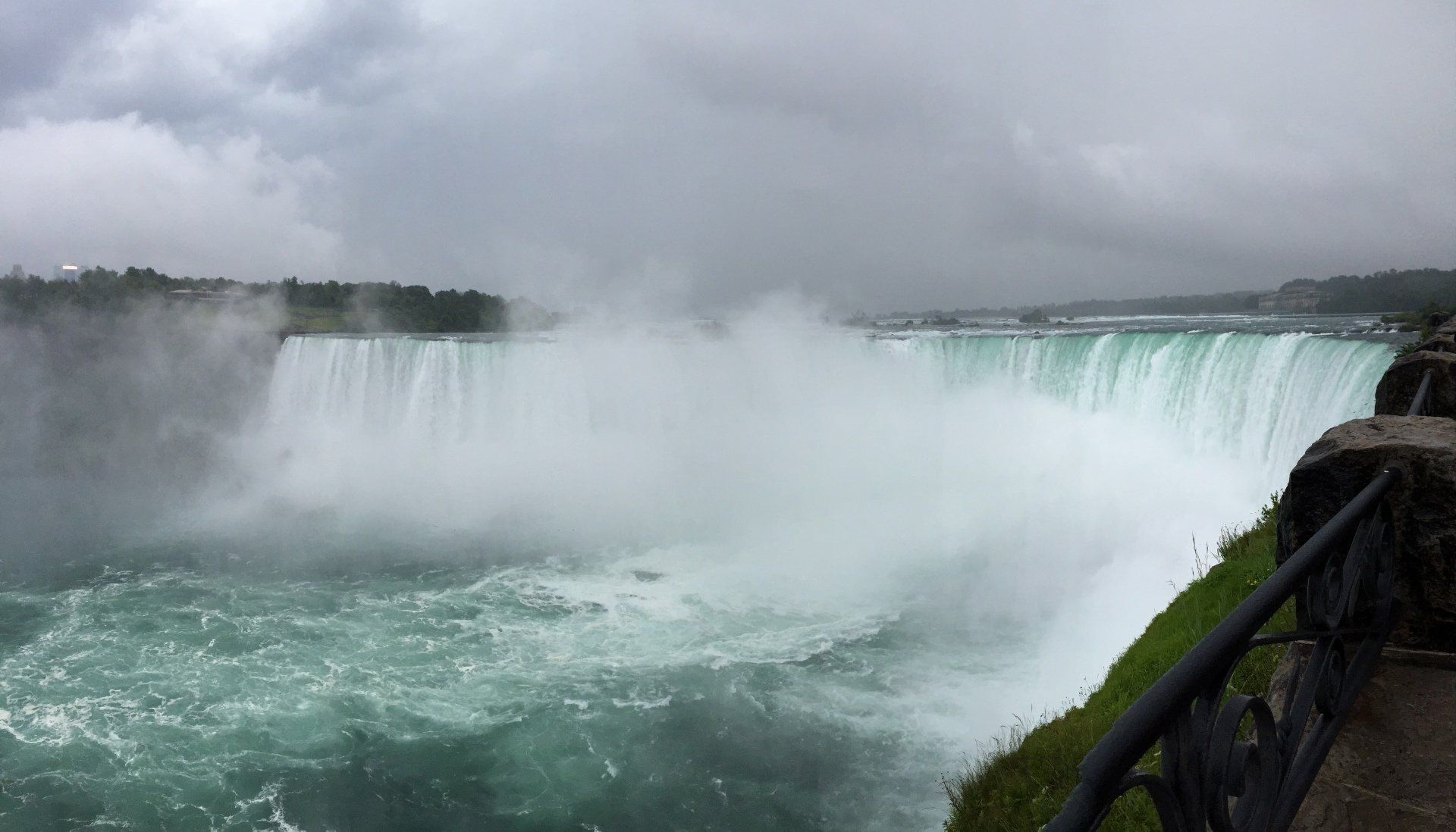 Een brede waterval met turquoise water stort neer over een klif onder een bewolkte hemel.