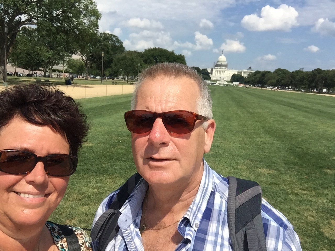 Twee mensen met zonnebrillen op maken een selfie op een grasveld met het Capitool van de VS op de achtergrond.