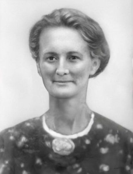 Zwart-wit portret van een vrouw met kort haar, gekleed in een jurk met patroon en een ketting, met een lichte glimlach.