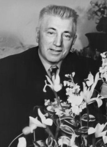 Man in pak poseert naast een boeket bloemen in een zwart-wit portret.