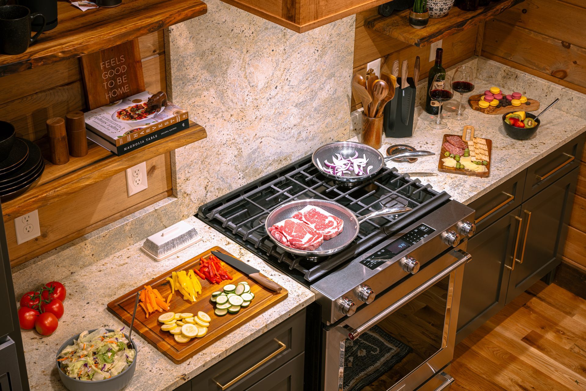An overhead view of a kitchen counter with raw steaks in a skillet, chopped vegetables on a board, and snacks.