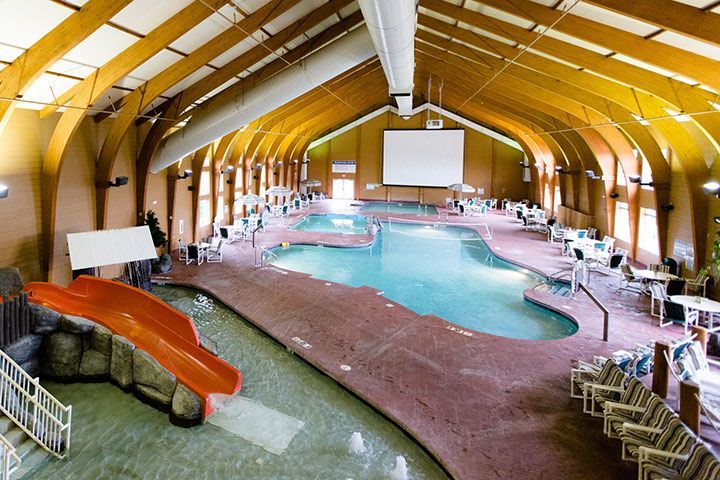 Indoor swimming pool with curved wooden ceiling, water slide, and lounge chairs.