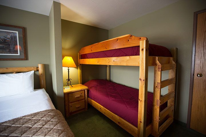 Bedroom with a bunk bed and a single bed. Green walls, wooden furniture, and a lamp.